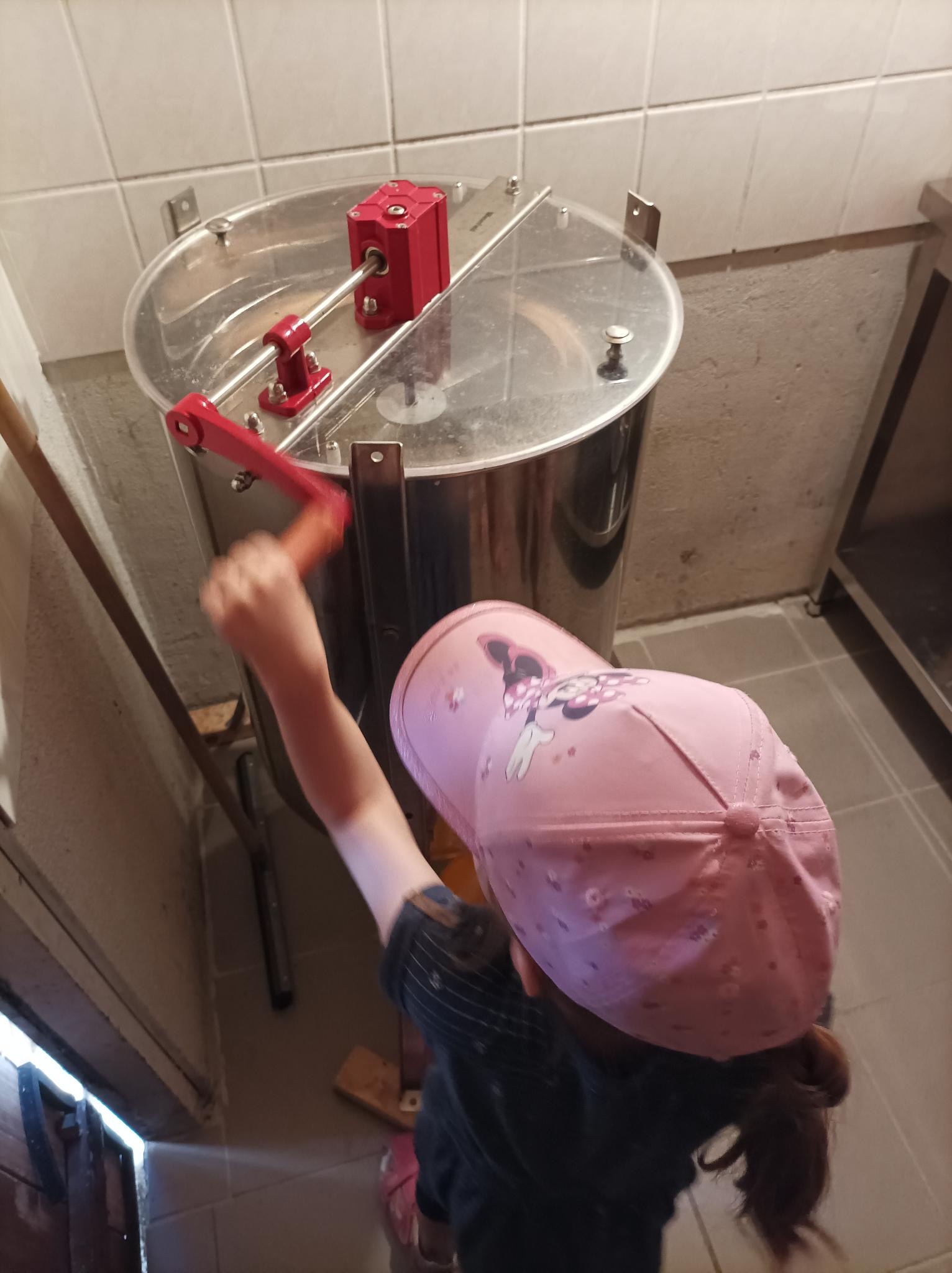 Ein Kind mit Mütze dreht an der Honigschleuder